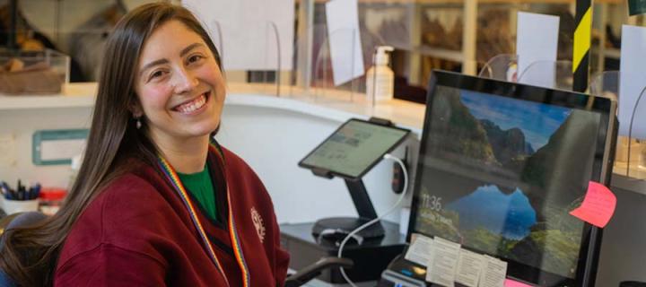 A staff member smiles to camera while working at a desk in The University Of Ųʿʷ¼ Visitor Centre